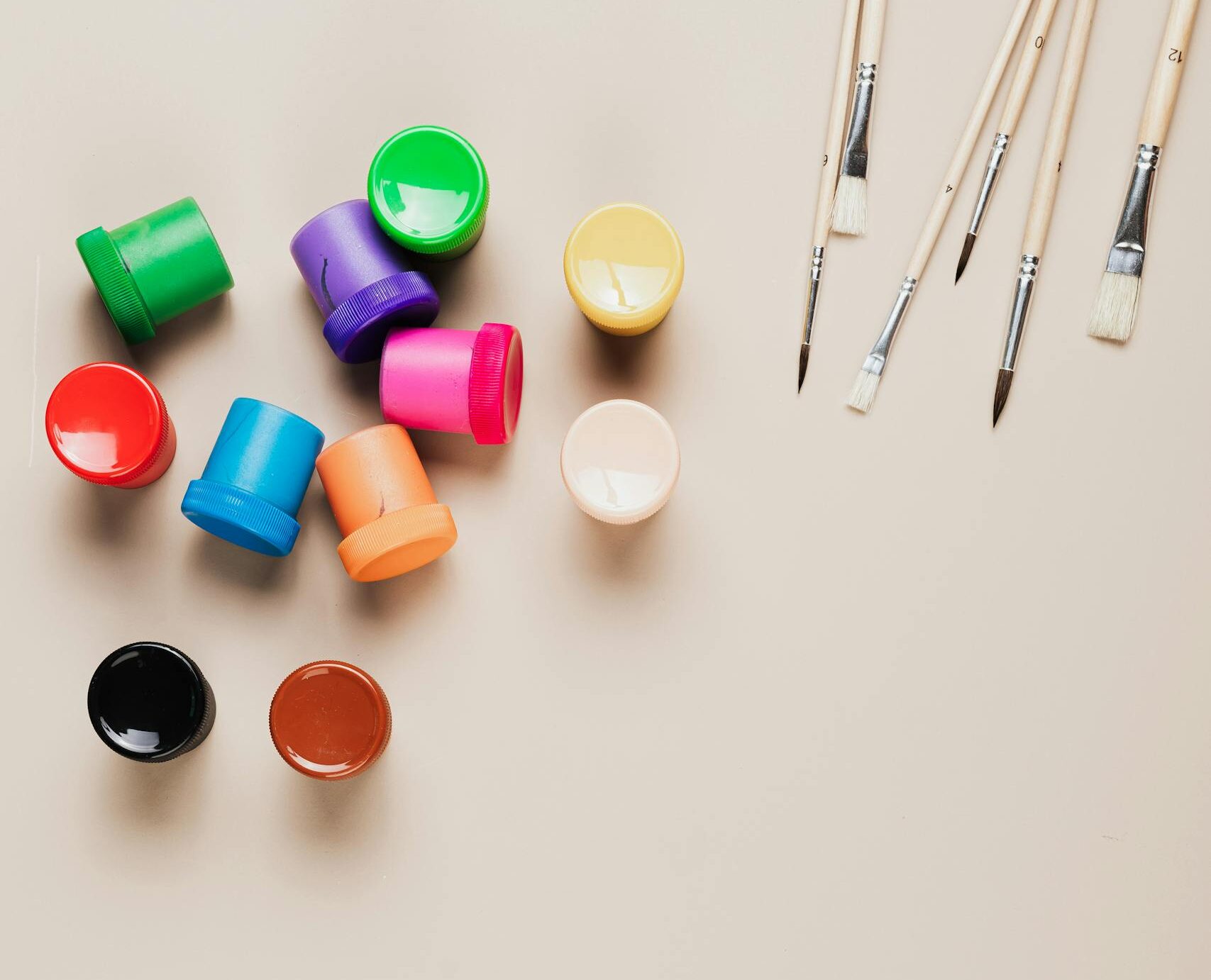 Flat lay of vibrant paints and brushes on a beige background with ample copy space.
